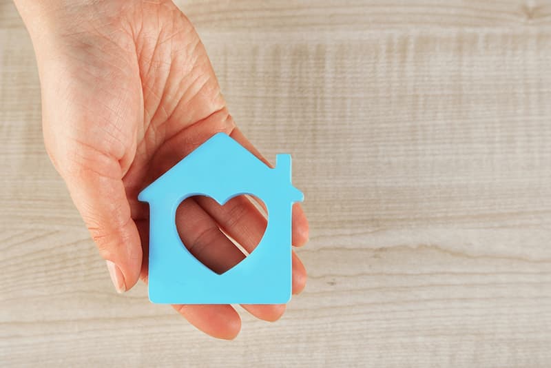 Hand holding a block shaped like a house with a heart cut out.